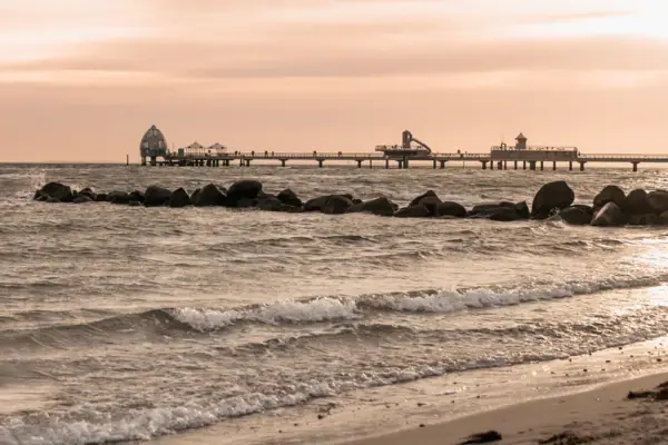 A beach with a jetty and rocks at sunset.