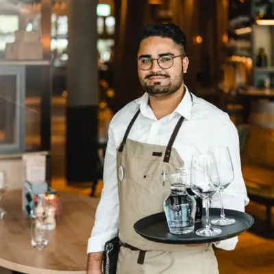 A man holds a tray with wine glasses and a bottle.