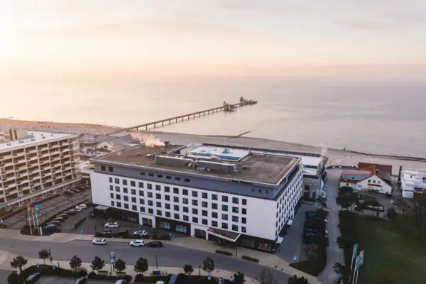 An aerial view of the white aja Grömitz building in the morning sun directly on the beach and the sea.