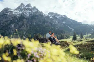 A man and a woman are sitting on a rock in front of a mountain.