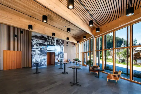 A large room with a wide window front, elegant furniture and exposed ceiling beams.