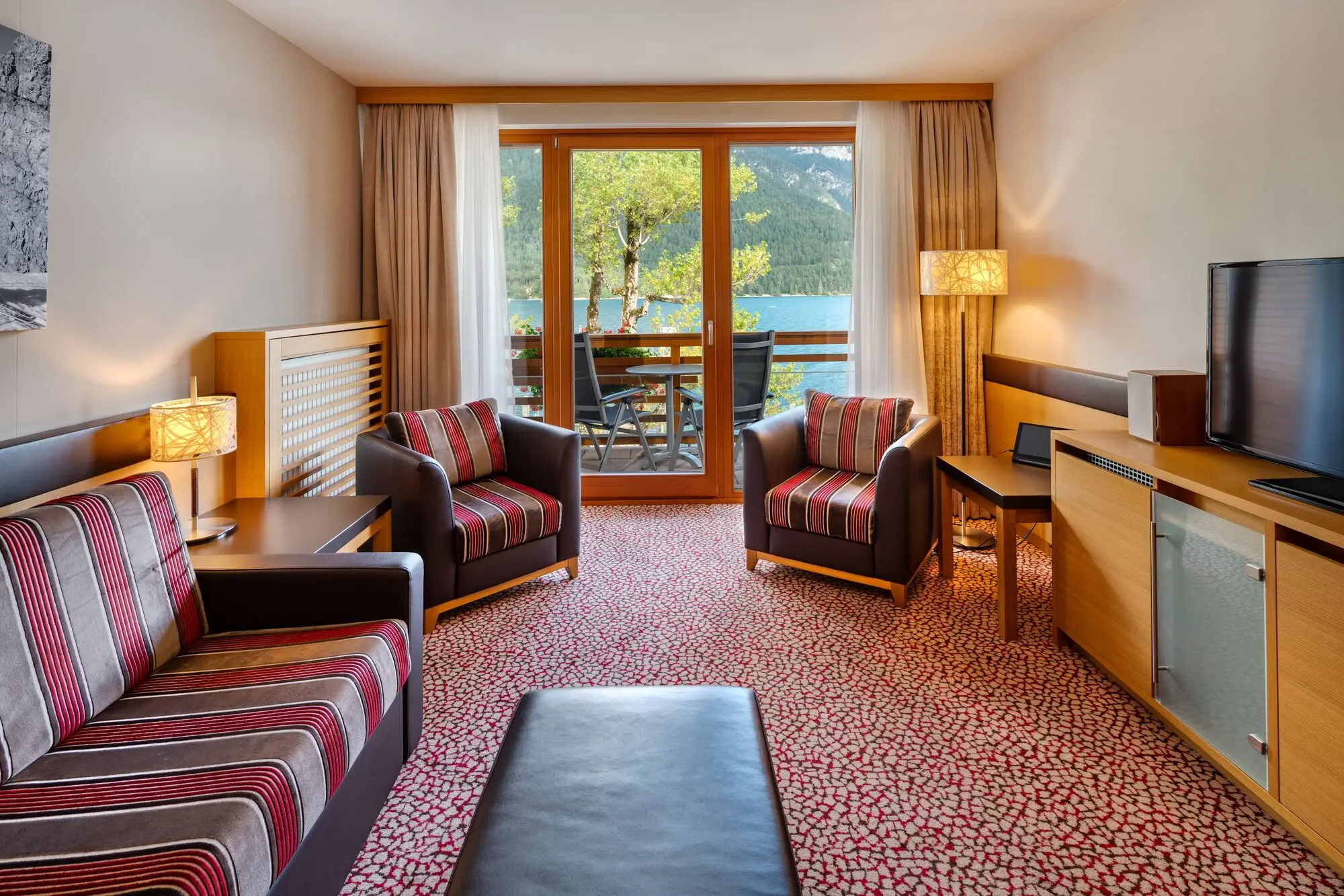 Living area of a hotel room with couch, armchairs, table and TV.