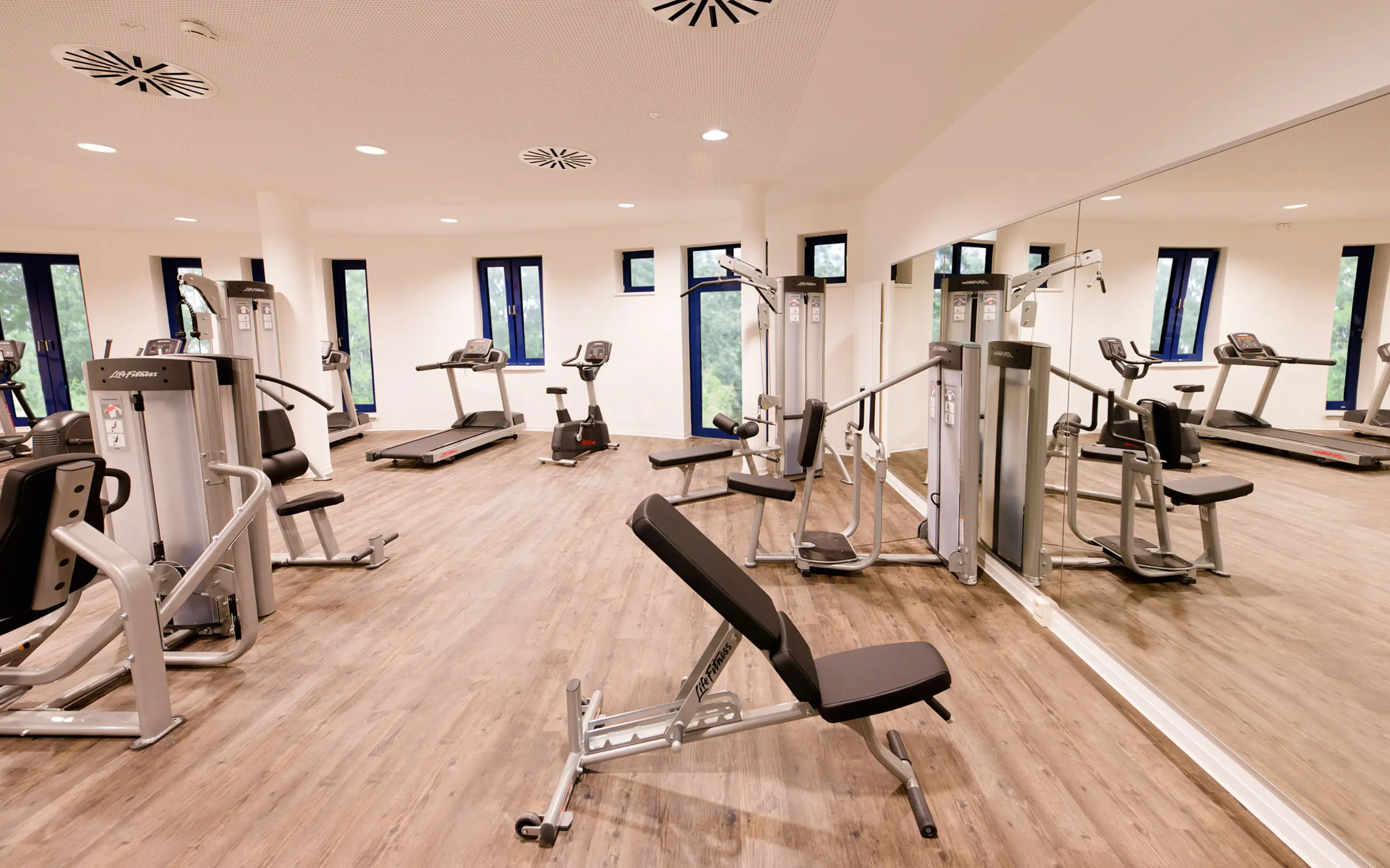 Modern fitness room with various workout machines, treadmills, and large mirrors, providing a bright and spacious environment for exercise.