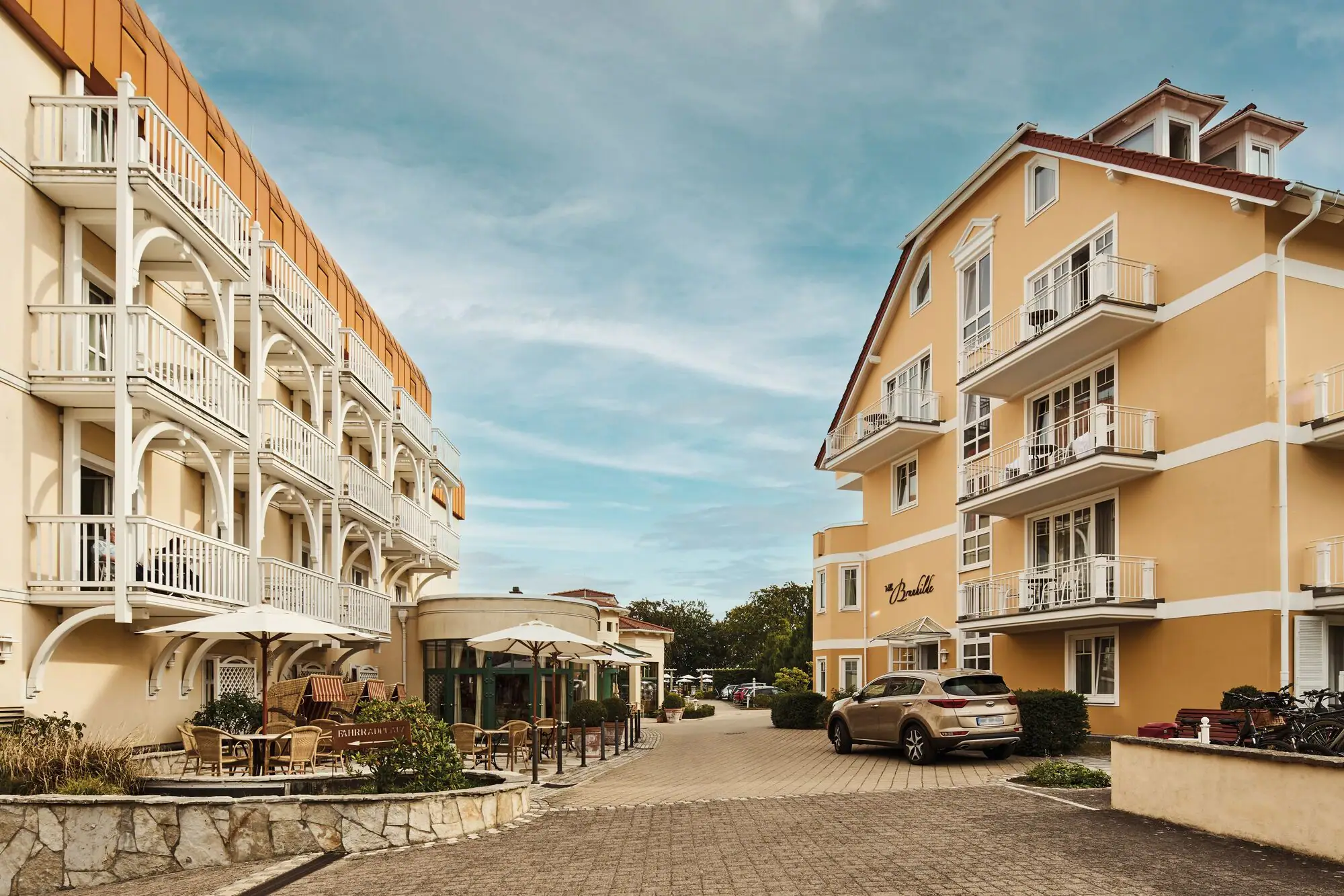 Street with buildings and parked cars outside under a cloudy sky.