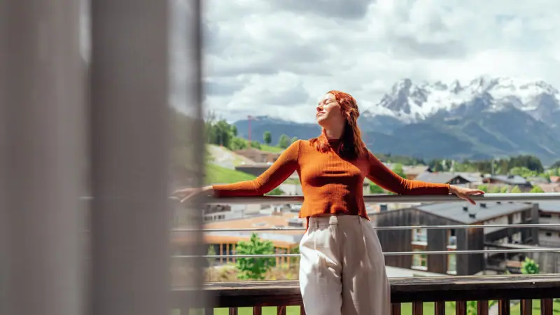A woman is standing on a balcony with her arms outstretched.
