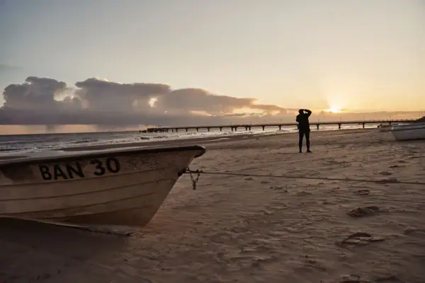 A person stands on the beach next to a boat.