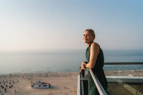 A woman leans against a railing overlooking a beach.