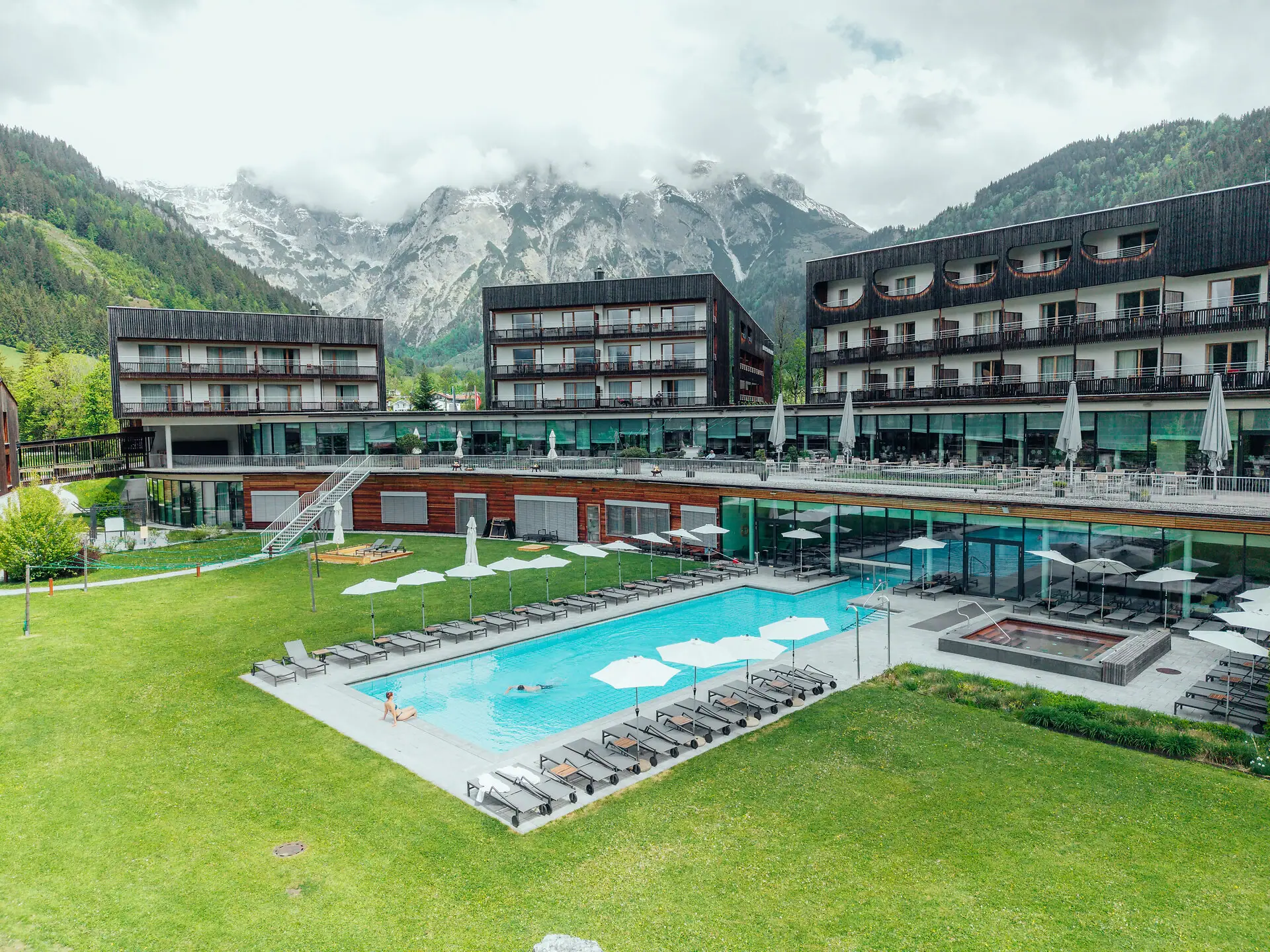 An outdoor swimming pool at a hotel, with a lawn and mountains in the background.