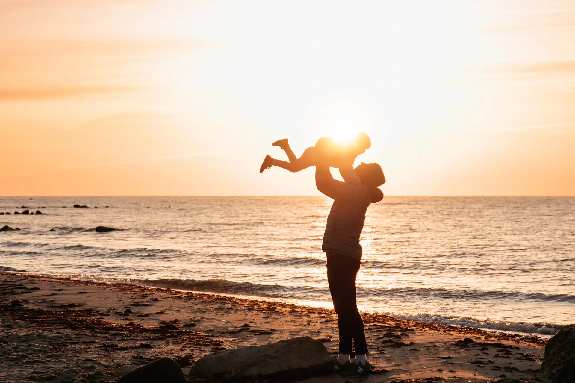 A woman holds a baby on the beach.