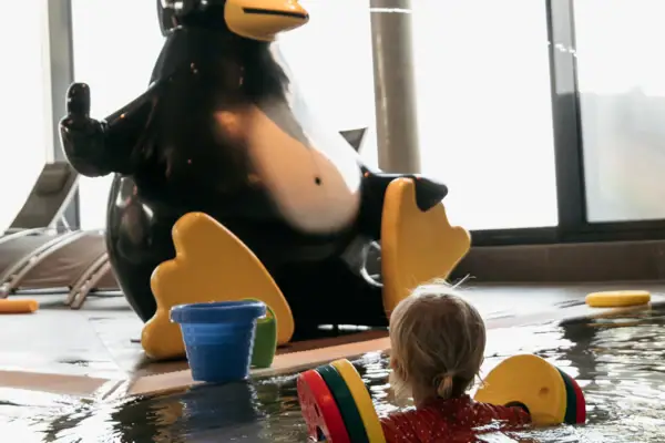 A child is swimming in a pool next to a penguin statue.