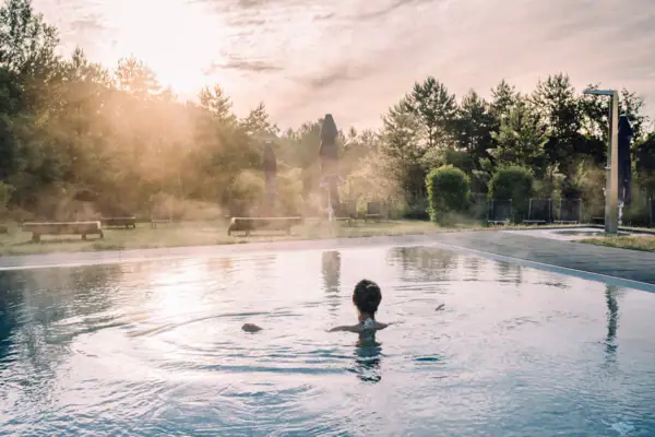 A woman in a pool with trees and a cloudy sky.