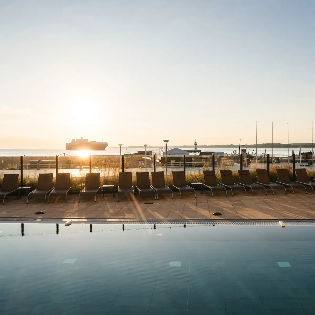A pool with chairs and a boat in the background.
