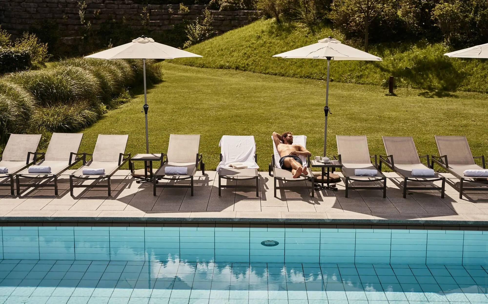 Man lying on a sun lounger next to a swimming pool.