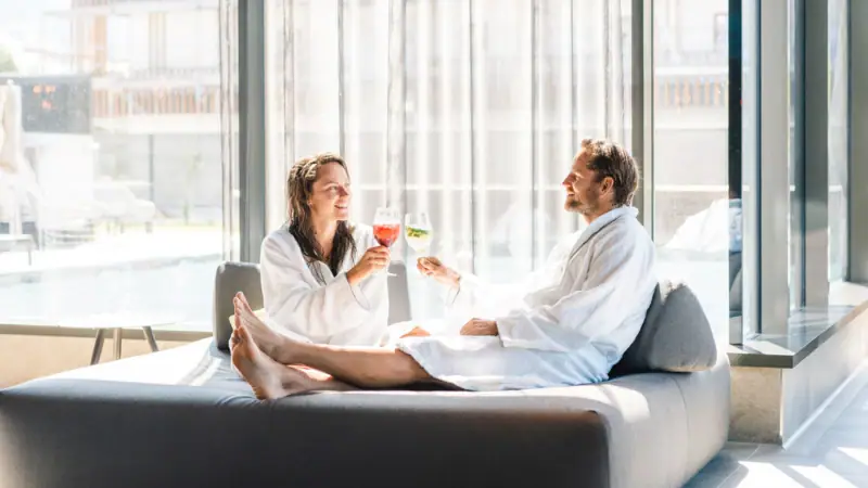 A man and woman in bathrobes sitting on a couch indoors.