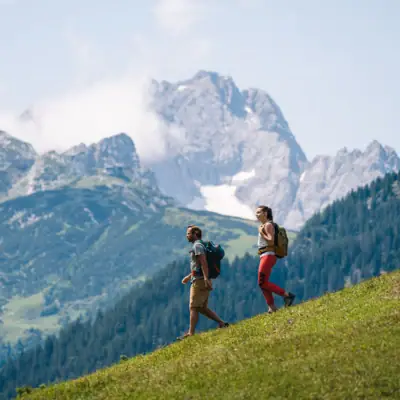 Two people hiking on a hill with mountains in the background.