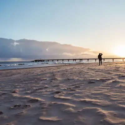 A person walks along the beach under a cloudy sky.