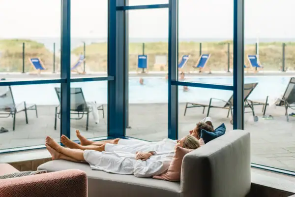 A couple lie on a wellness sofa with a view of the outdoor pool.