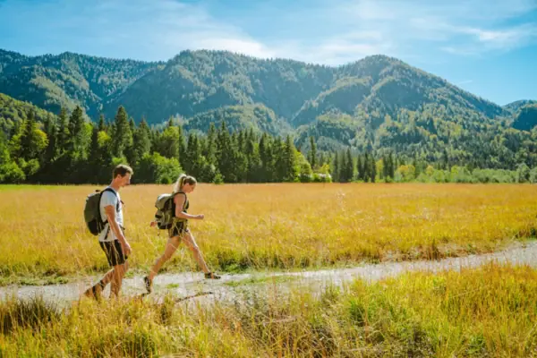 Hiking in Ruhpolding A man and a woman walk in a field with mountains in the background.