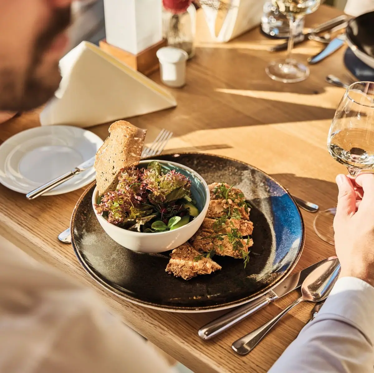 Feinspitz Restaurant Man eats salad and drinks a glass of wine at the table.