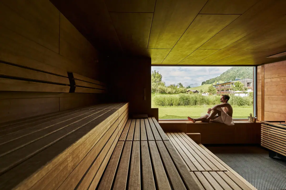 A man sits on a bench in a sauna with a window.