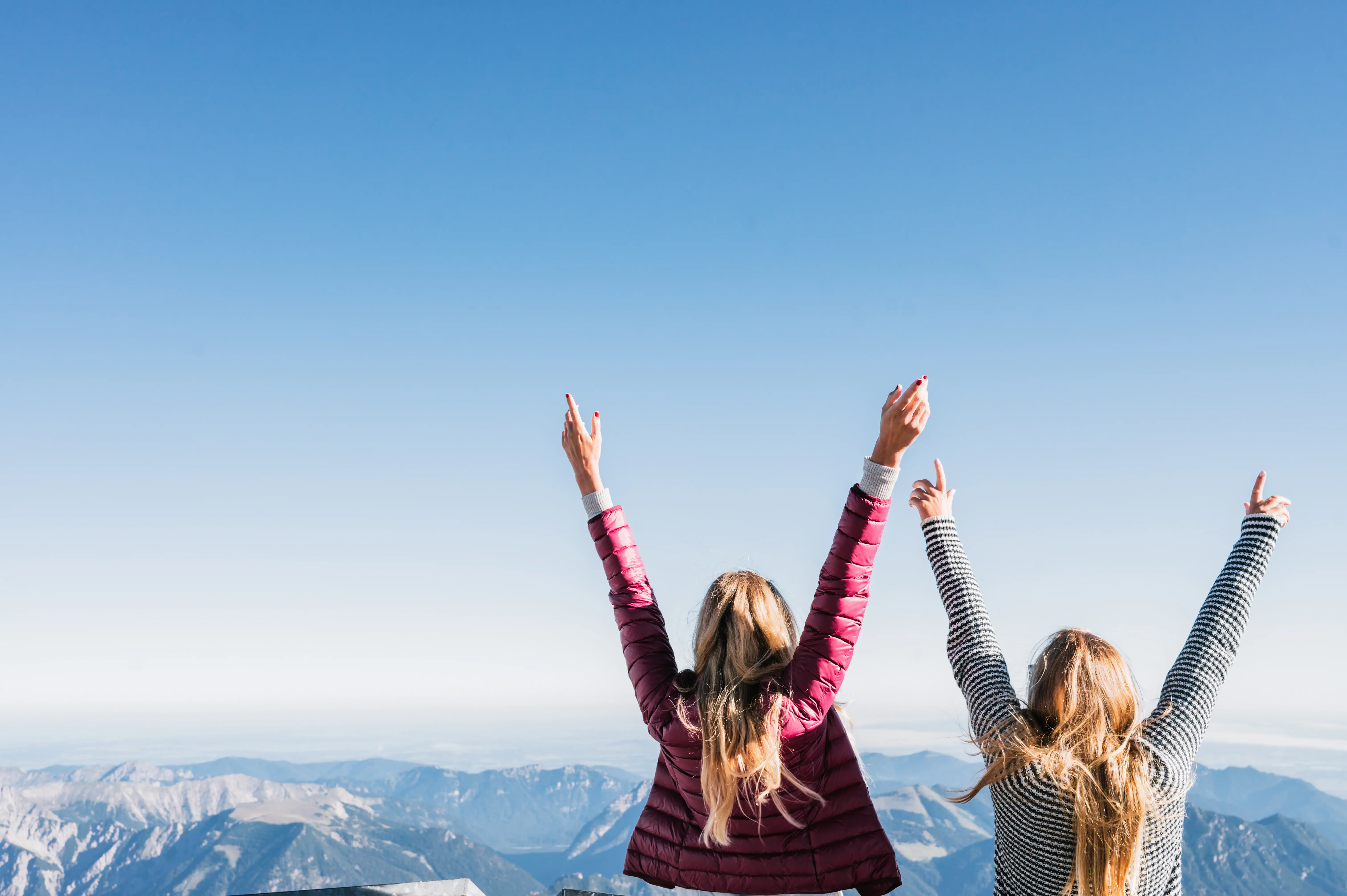 Two women are standing on a mountain with their arms raised.