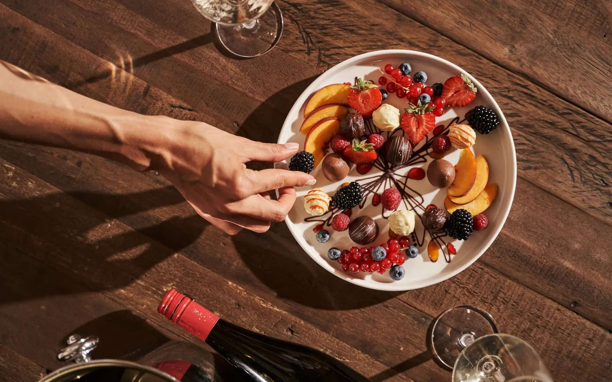 Hand reaches for a plate of fruit on a table.