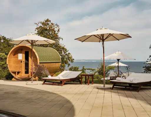 Outdoor wellness area Deck chairs and parasols next to a barrel and a body of water.
