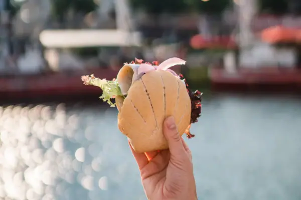 One hand holds a fish roll over glistening water.