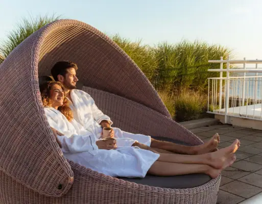 Wellness A man and woman in white robes sitting in a wicker chair outdoors.