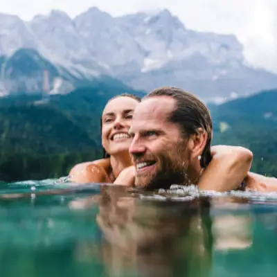 A man and a woman in the water against a mountain backdrop.
