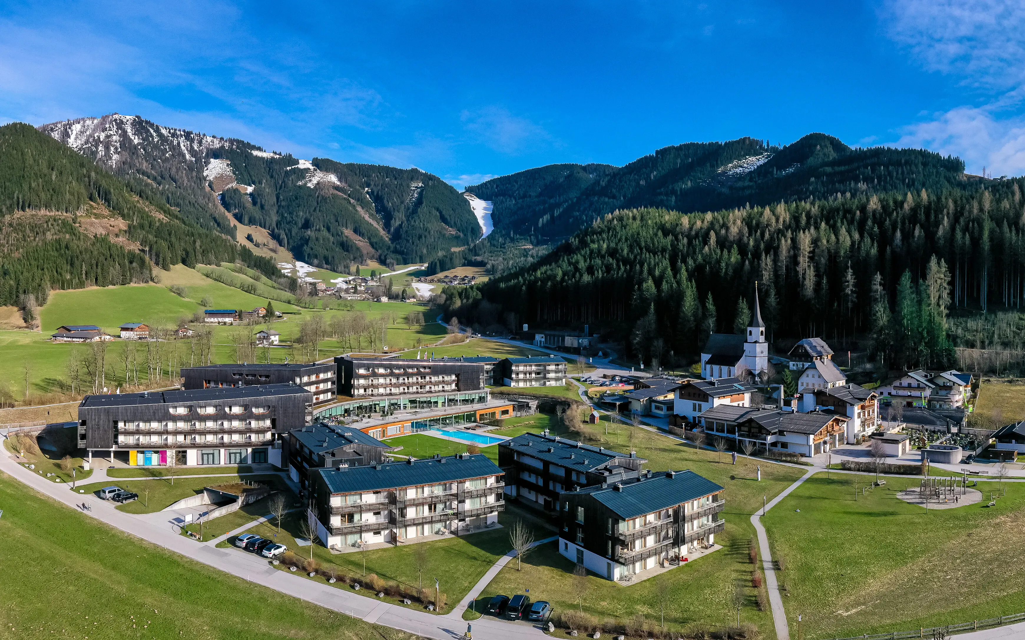 A group of buildings in a valley with mountains and a partly cloudy sky in the background.