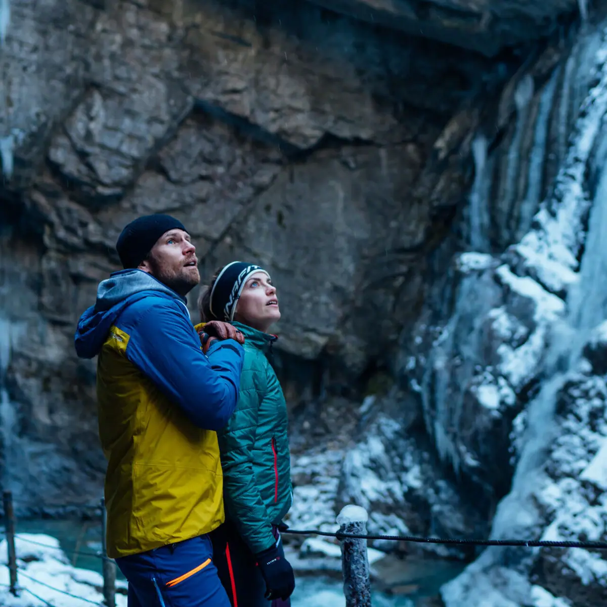 A man and a woman are standing in the Partnach Gorge, surrounded by a wintry landscape.