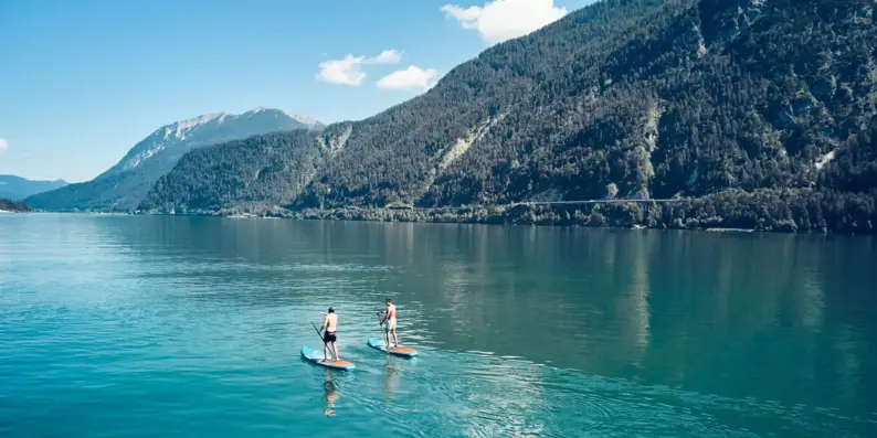 Two people on paddleboards on a lake with mountains in the background.