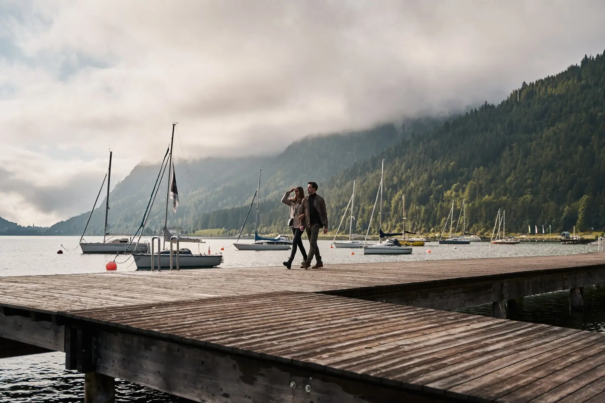 Boats on the Achensee A couple walks on a jetty with boats in the background.