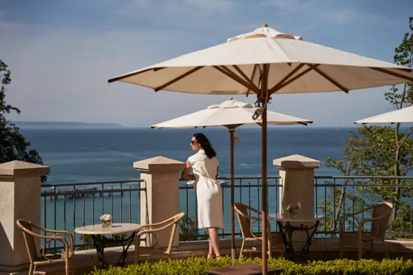 A woman in a white dress stands on a railing with a large umbrella.