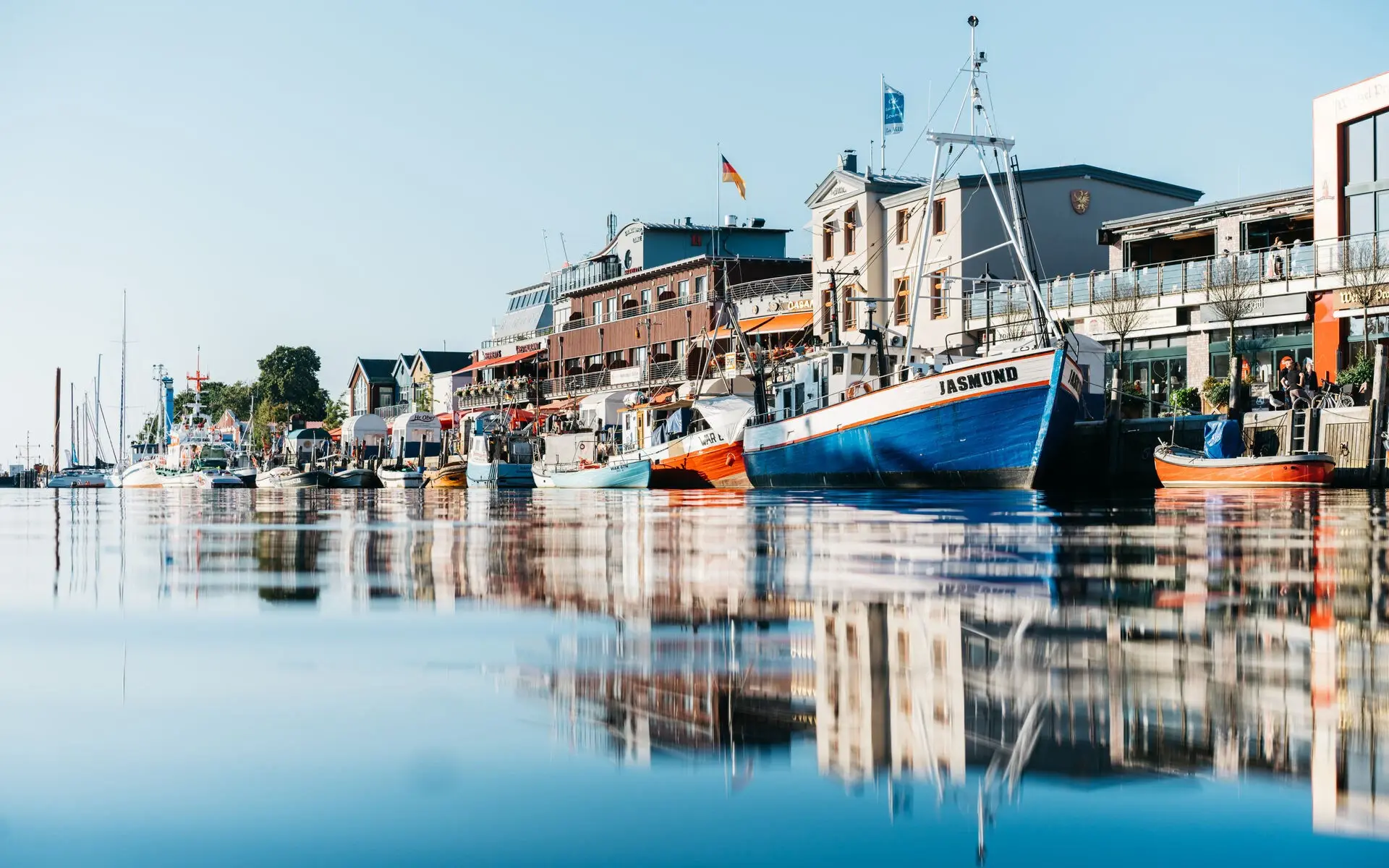 A small harbour area with moored boats and shops in the background on a sunny day. 