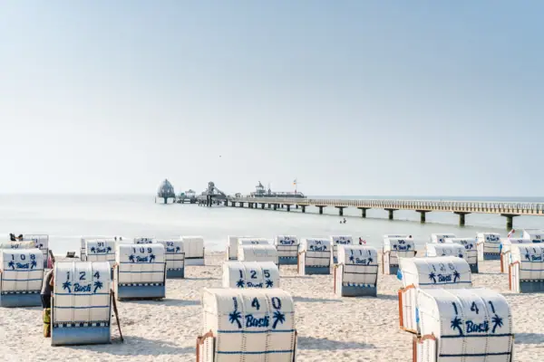 A beach with white beach chairs and blue stripes against a clear sky.