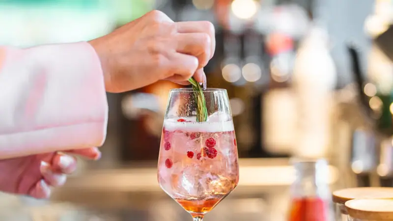 A person placing a leaf on a drink in a wine glass.