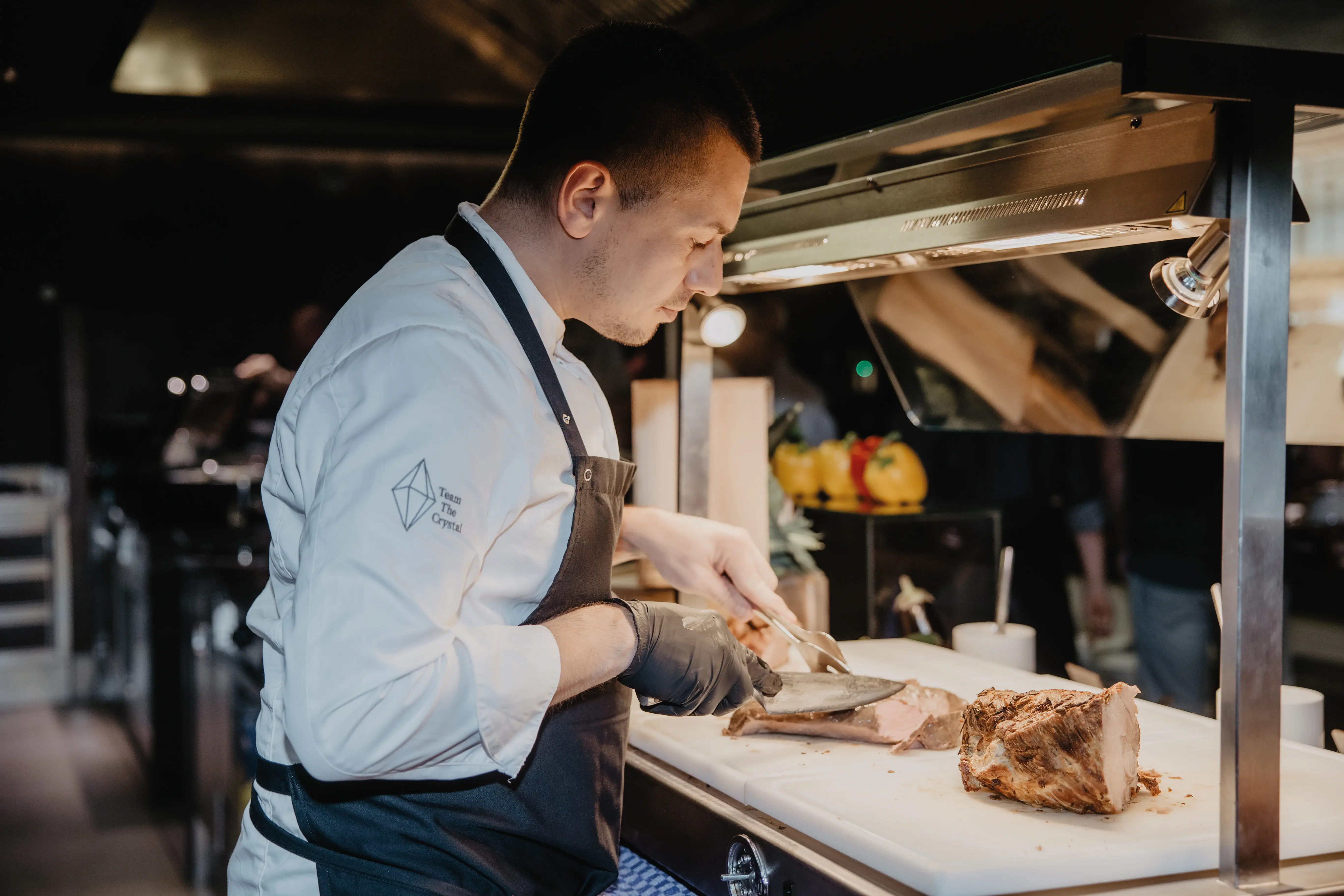 A man in a chef's uniform cuts meat.