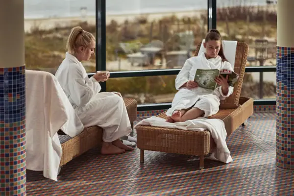 Two women in white bathrobes sit on deckchairs.