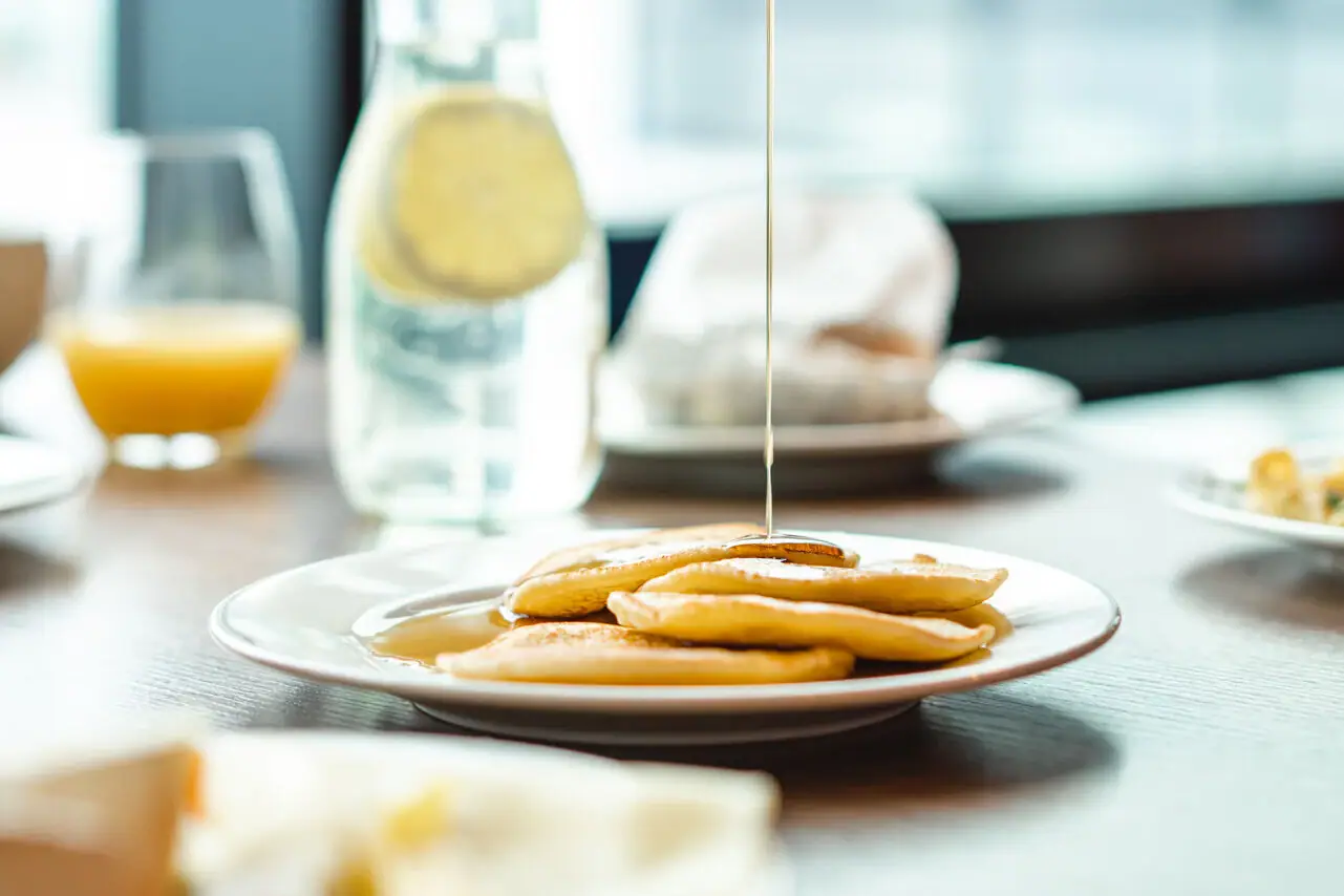 One person pours syrup onto a plate of pancakes.