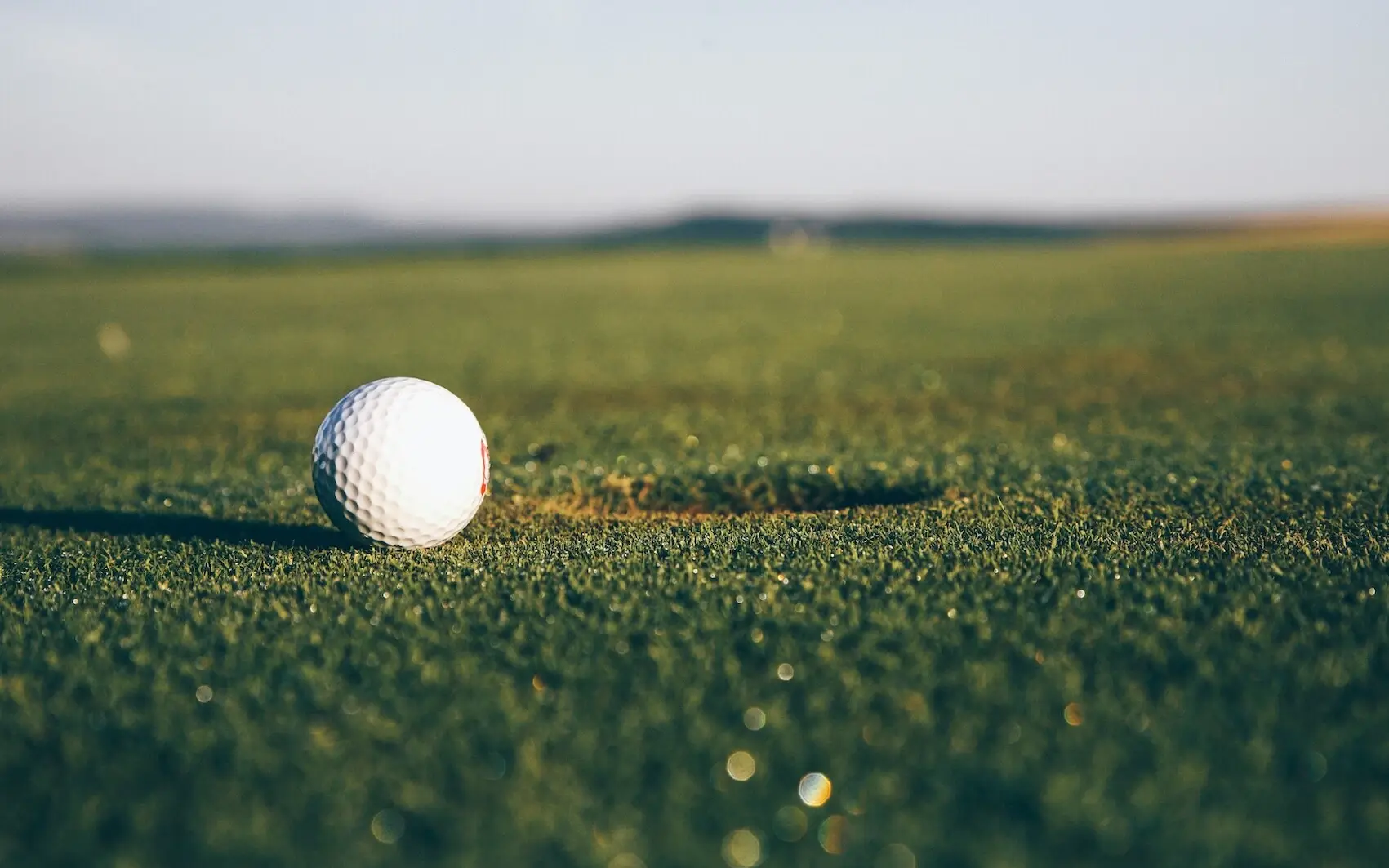 Ein Golfball liegt auf dem Rasen vor einem Loch.