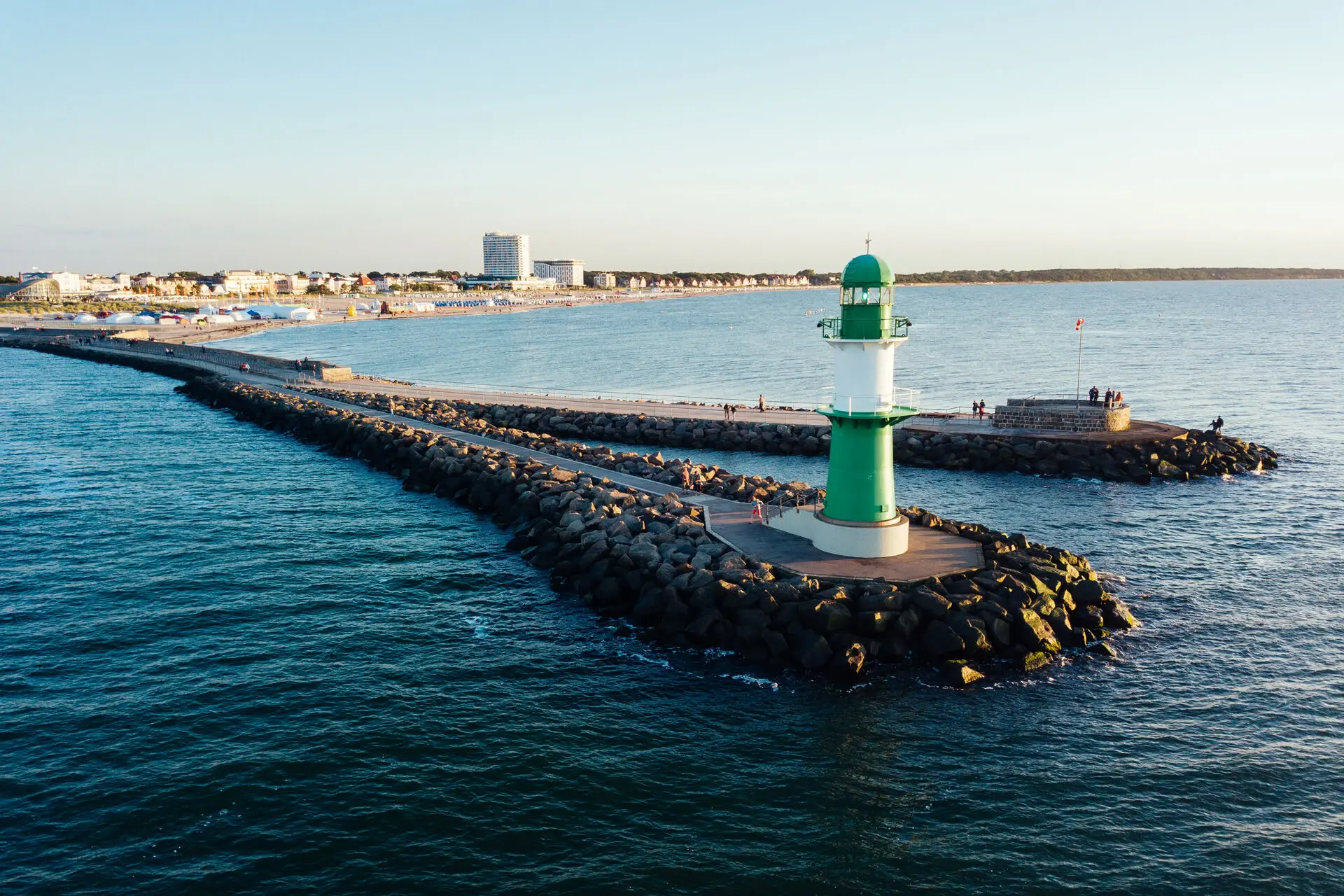 Warnemünde lighthouse Green and white lighthouse on rocks in the water.