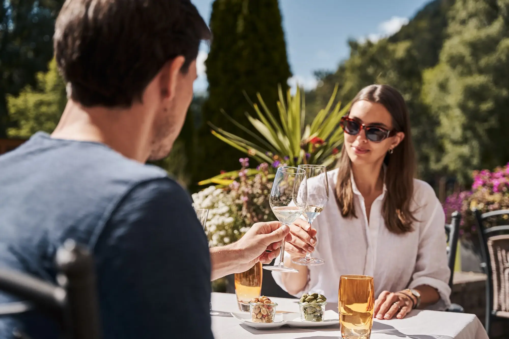 A man and a woman clink glasses of wine at an outdoor table. 