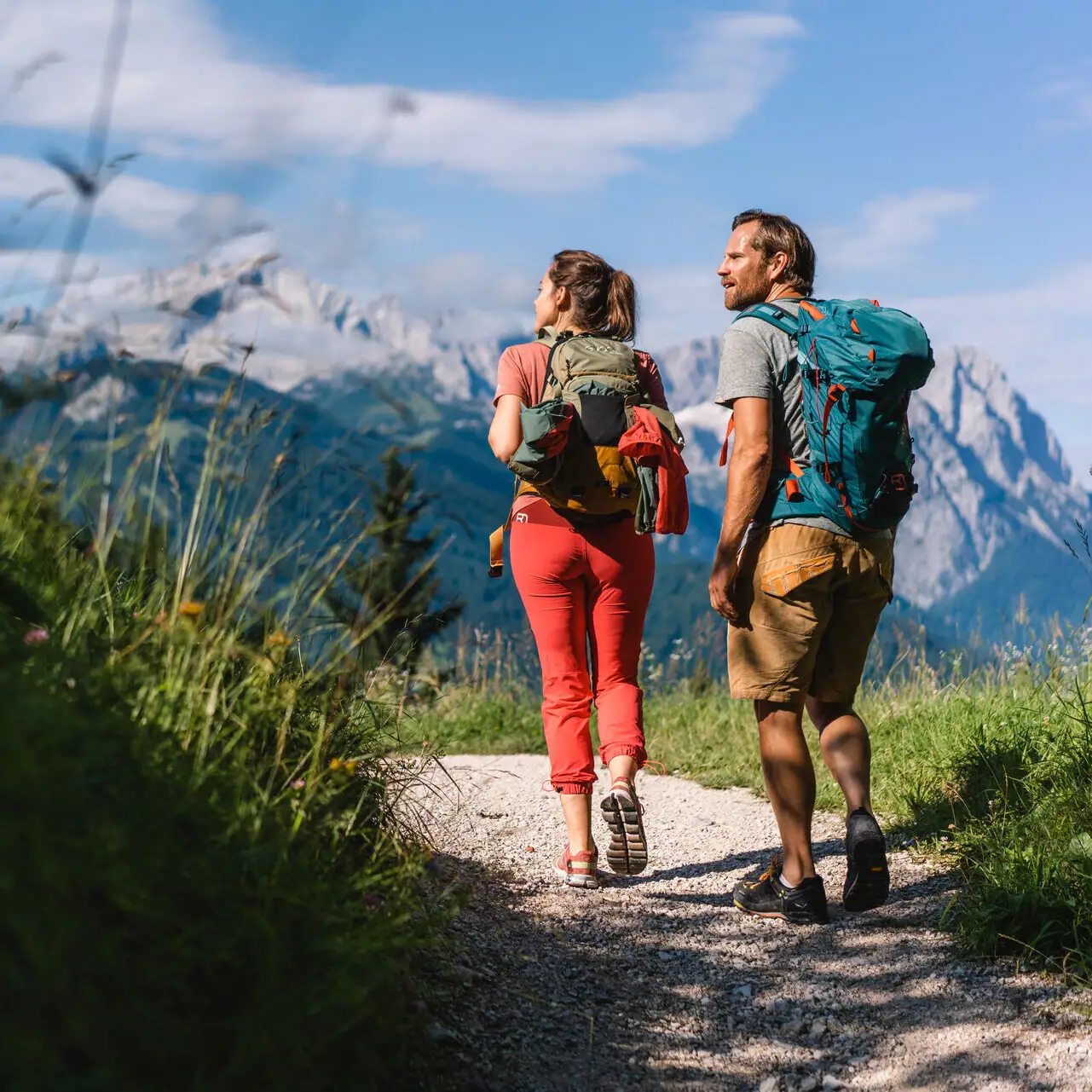 Hiking A man and a woman walk along a path with mountains in the background.