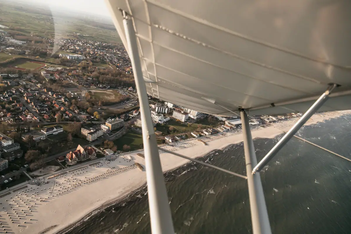 An aeroplane wing above a beach, with buildings in the background.