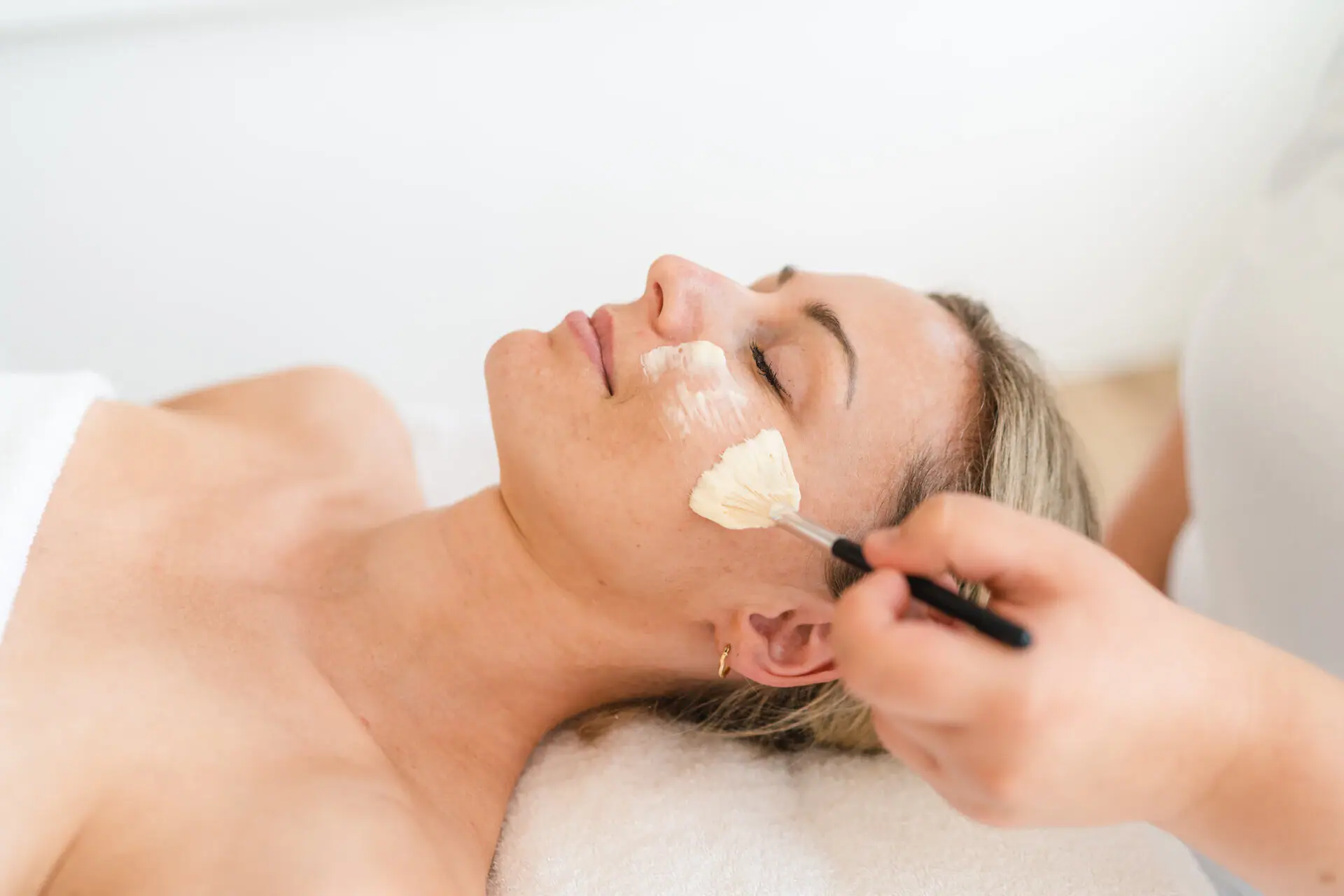 A woman lies on the couch with a brush on her face and receives an application.