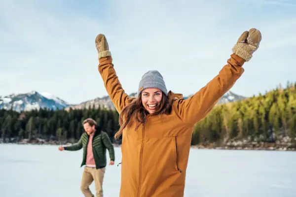 A woman with her arms raised stands in front of a man in a snowy field.
