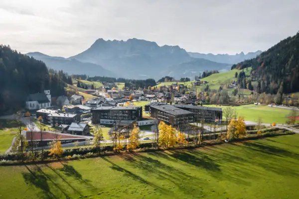 Town in a valley with mountains in the background, surrounded by grassland and trees.