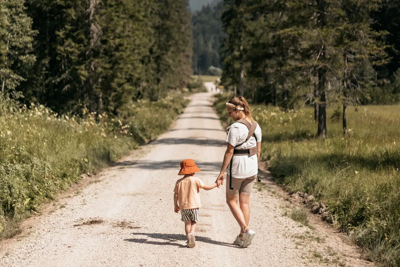 Hike with a child A woman and a child are walking along a country lane with trees.